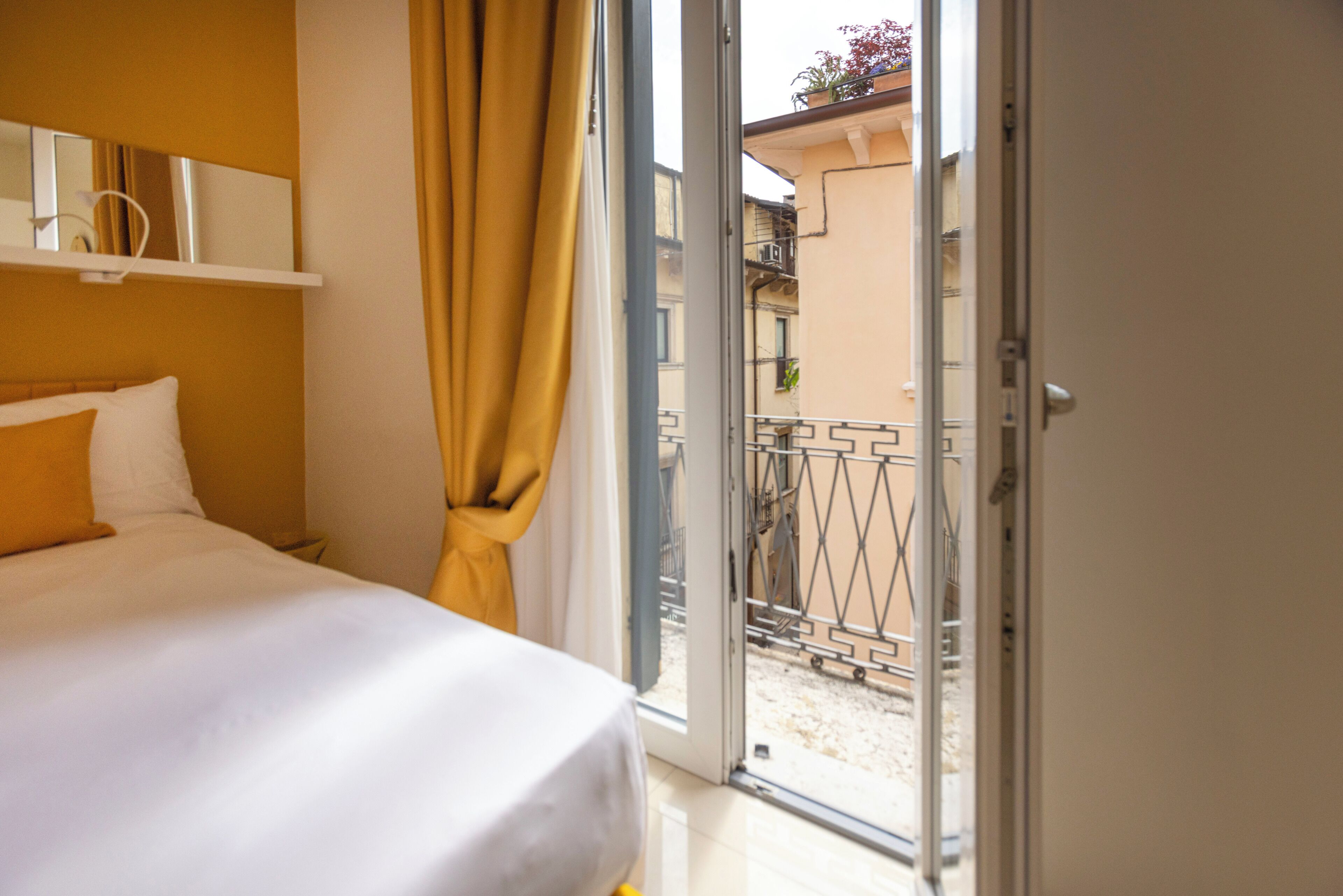Una habitación de hotel con cama, cortina y puerta abierta a un balcón.