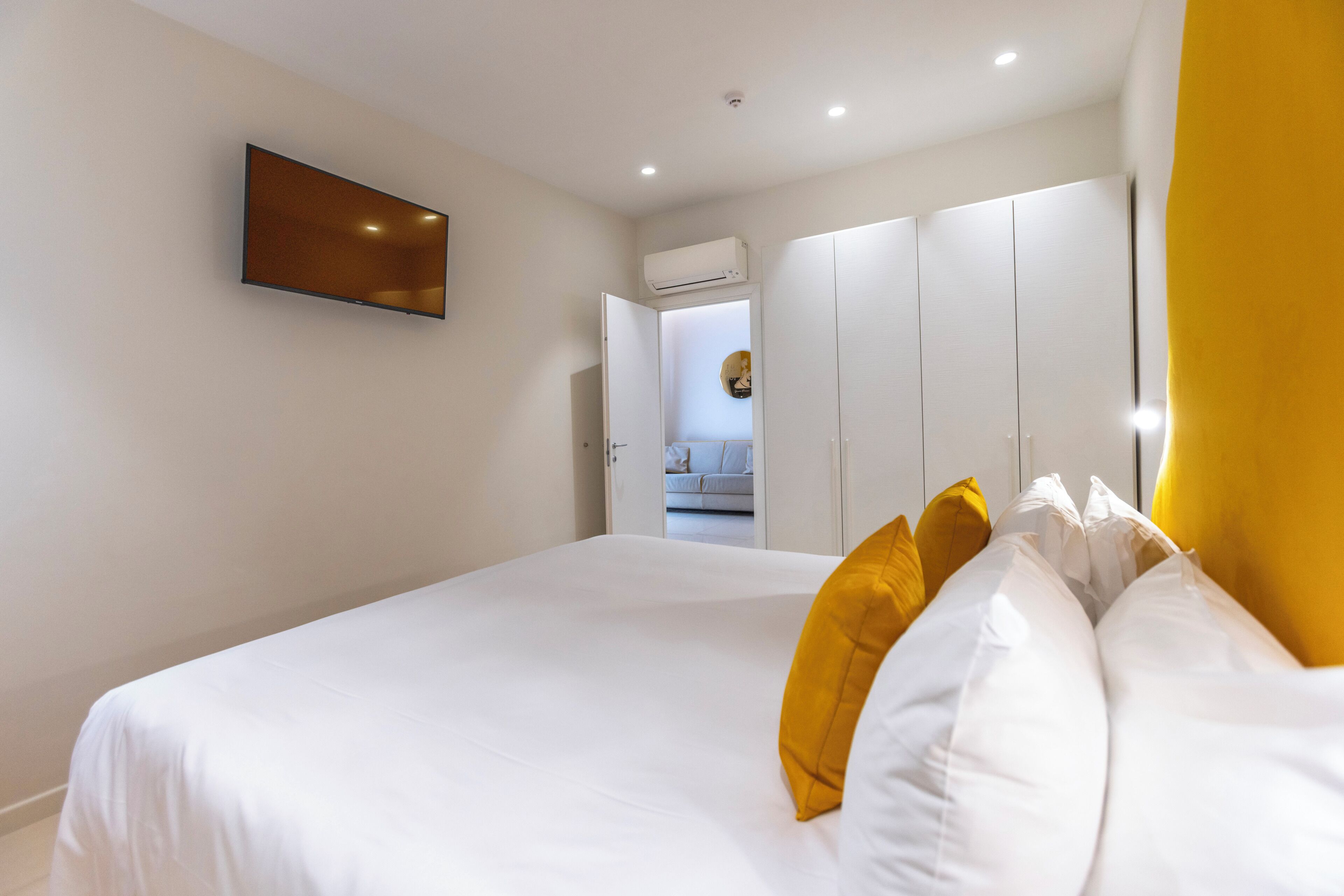 Un dormitorio con cama, televisor montado en la pared y armario con puertas abiertas.