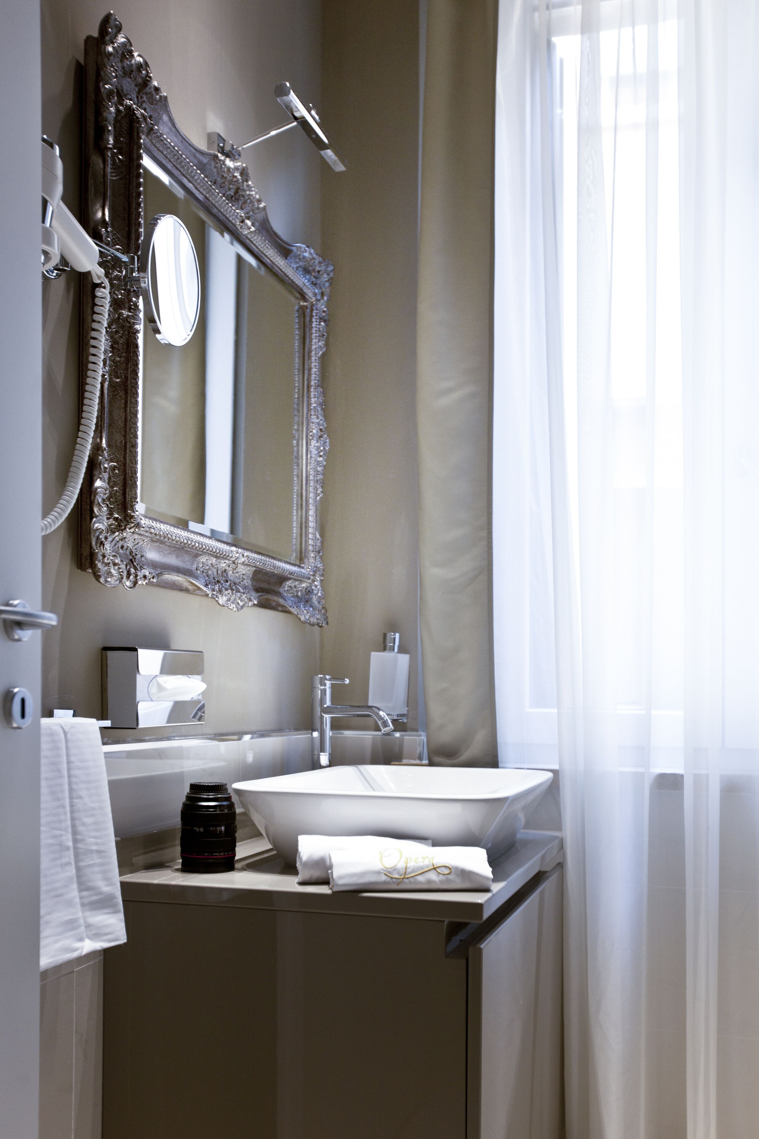 Un baño con un espejo grande y ornamentado, un lavamanos blanco y una ducha.