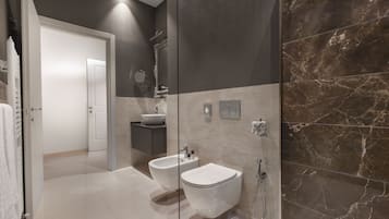 Un baño moderno con bidé, inodoro y zona de ducha con mampara de vidrio.