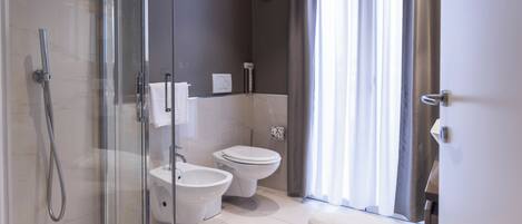 Une salle de bain moderne avec une douche à parois de verre, un bidet, des toilettes et un porte-serviettes.