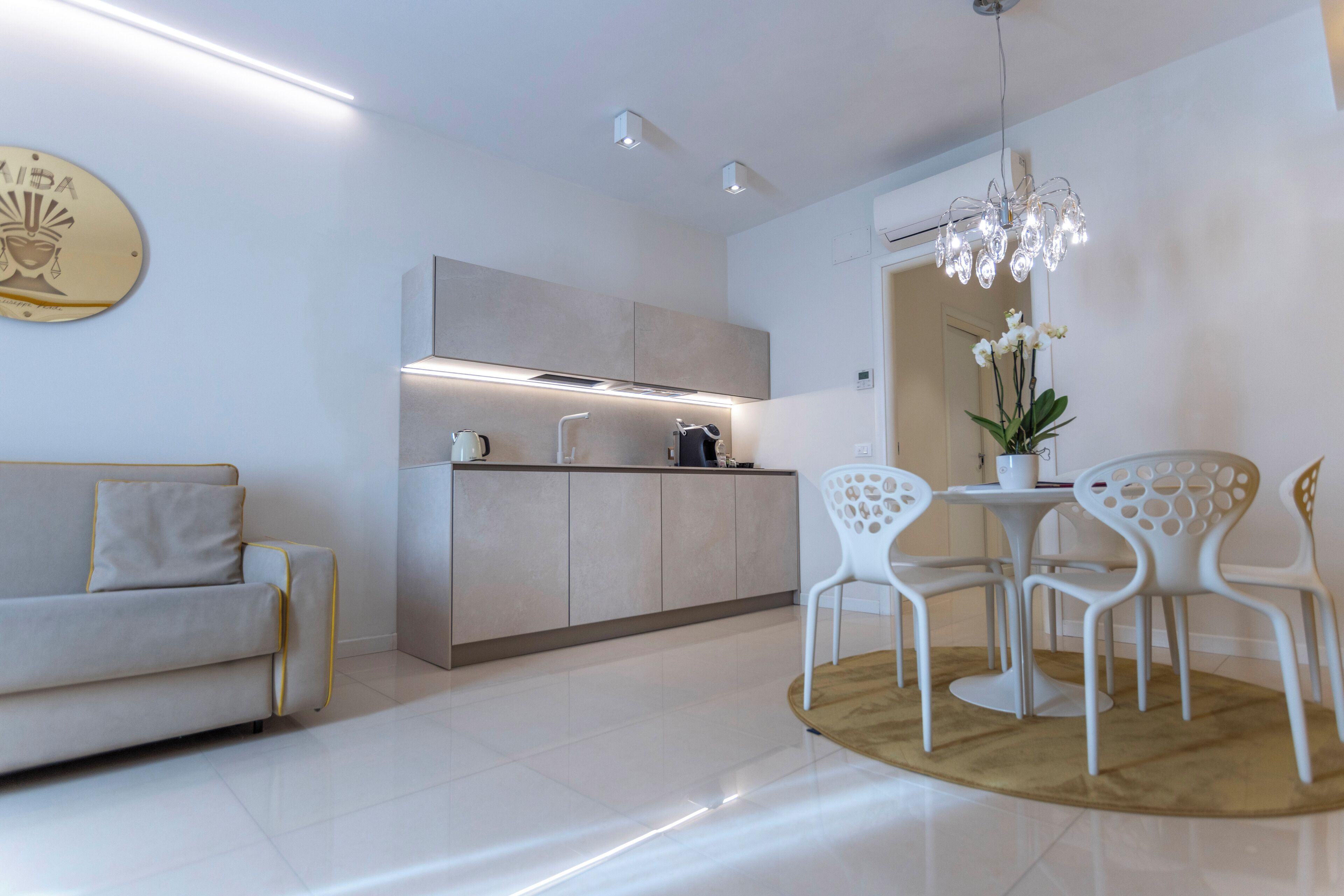 A modern kitchen with a built-in oven, a dining area with white chairs, and a sofa.