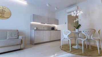 A modern kitchen with a built-in oven, a dining area with white chairs, and a sofa.