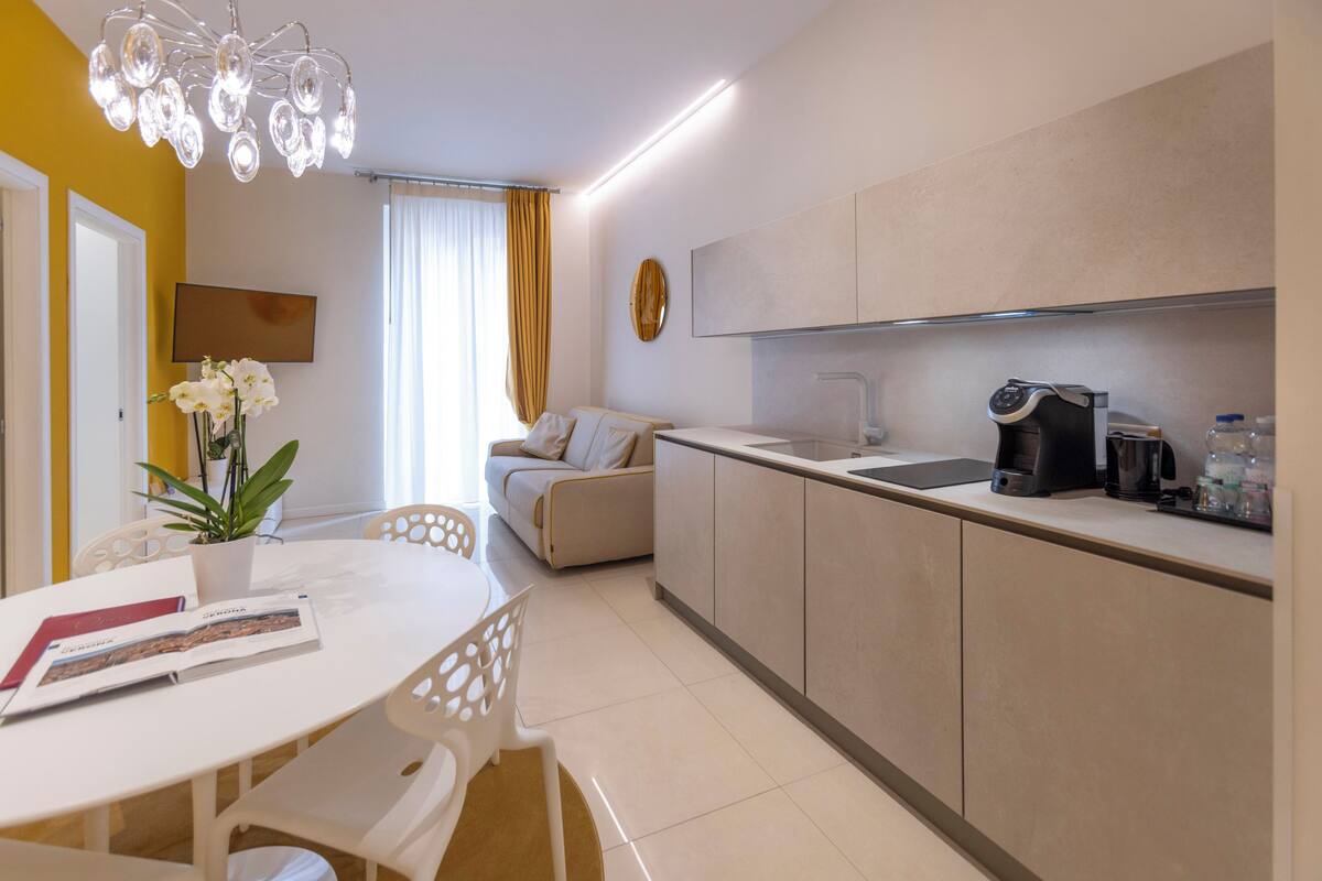 A modern kitchen with a dining area, a sofa, and a plant.