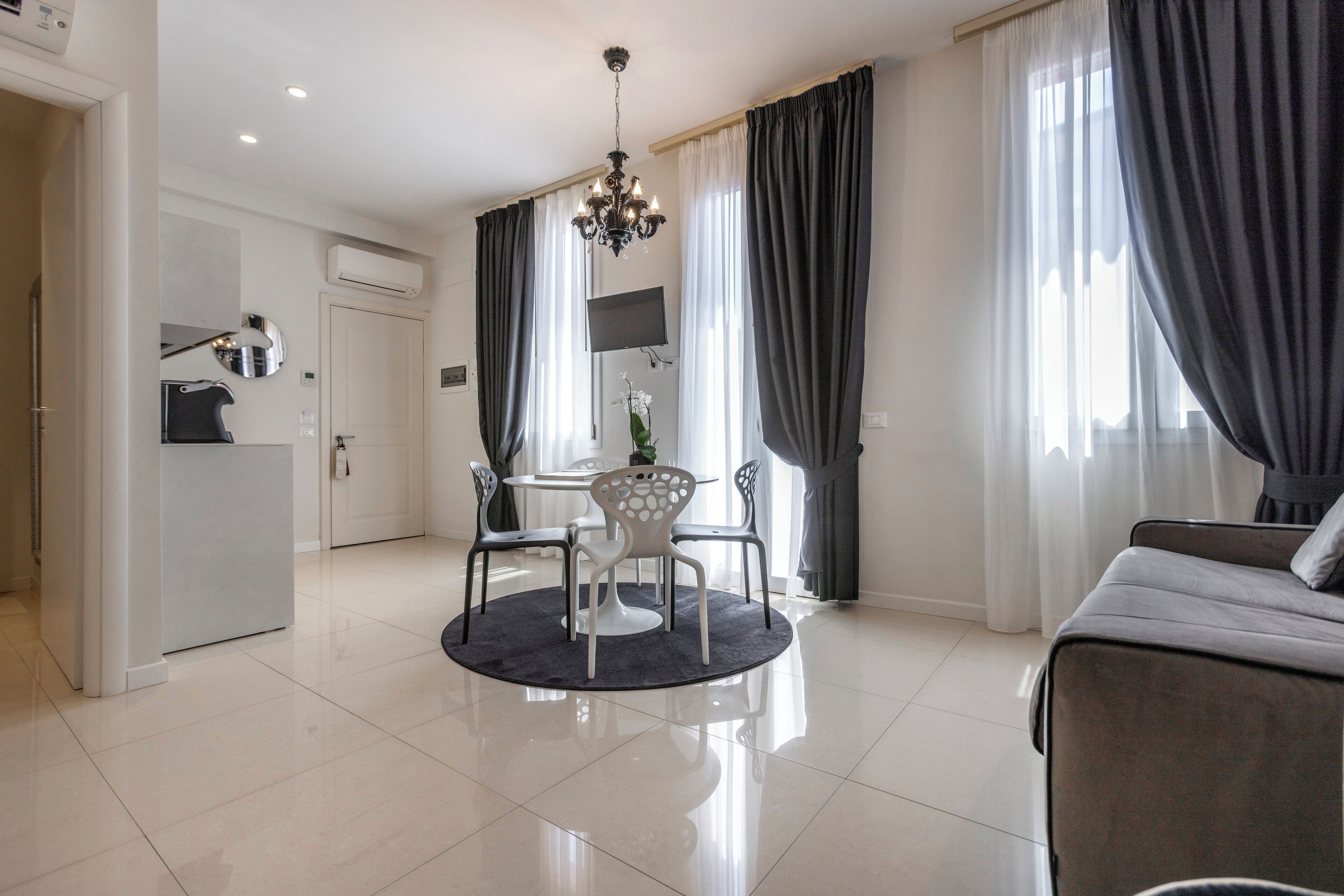 A modern living room with a round table, four chairs, a sofa, and a chandelier.