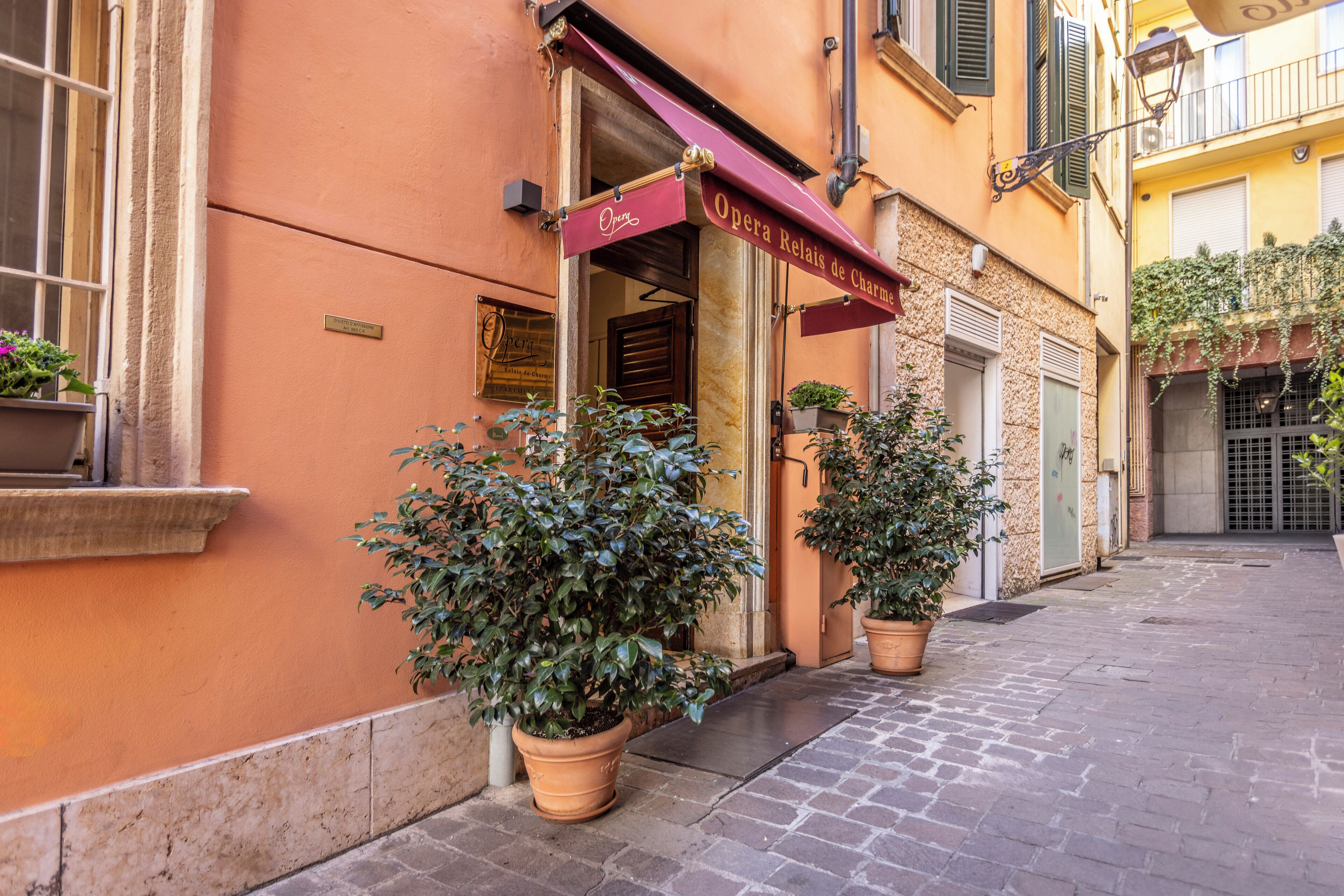 A building with an 'Opera Relais de Chambre' sign, potted plants, and a cobblestone street.