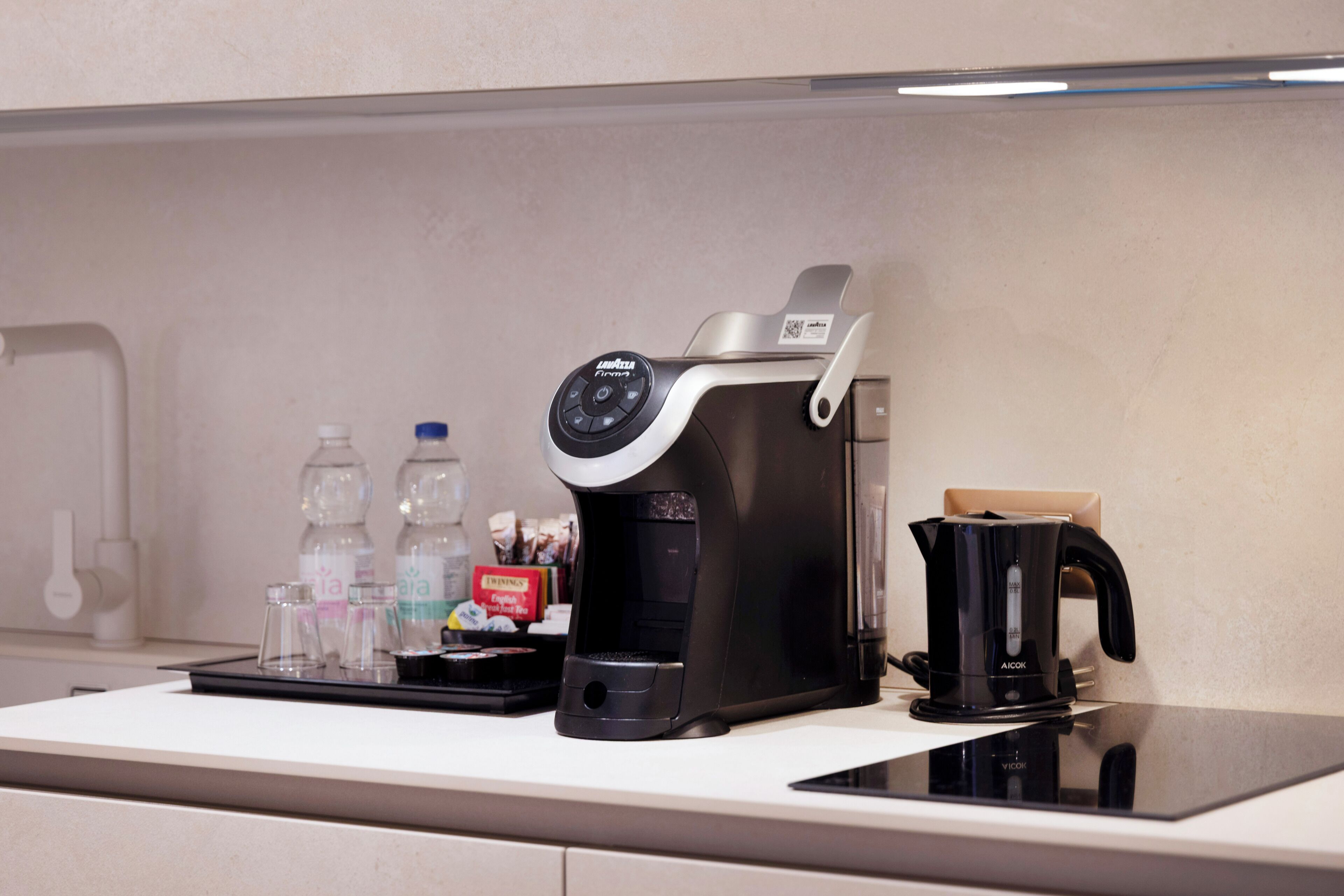 Una cocina con cafetera, hervidor y una bandeja con botellas y una caja.