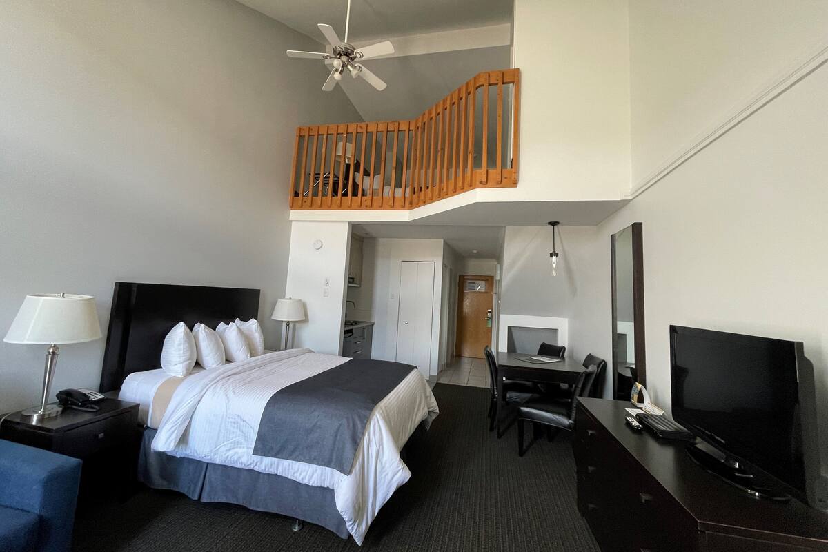 Een hotelkamer met een bed, bureau, televisie en een balkon met houten leuning.