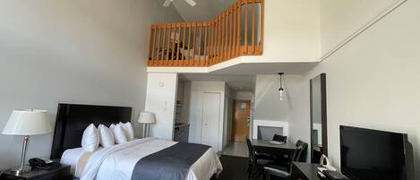 Habitación de hotel con cama, escritorio, televisión y balcón con baranda de madera.