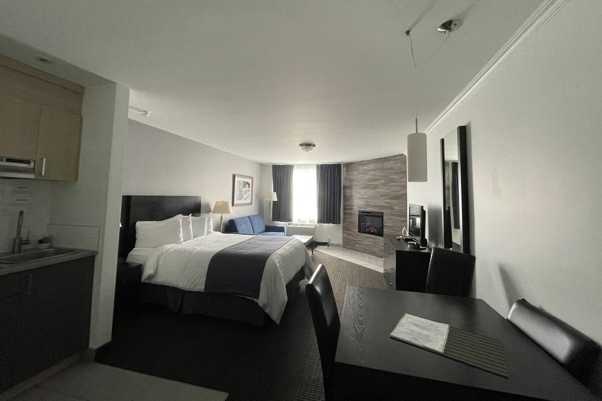Een moderne hotelkamer met een groot bed, een bureau met stoel, een flatscreen televisie en een klein keukentje.