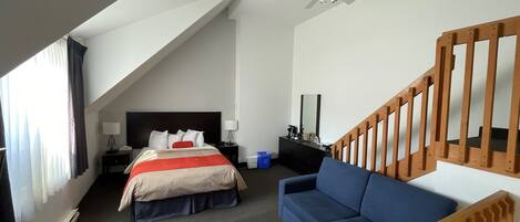 Une chambre d’hôtel avec un lit, un canapé bleu, un escalier en bois, un ventilateur de plafond et une table de chevet avec une lampe.