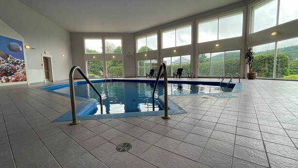 Piscina interior con vistas despejadas al exterior gracias a amplios ventanales, suelo de baldosas y una escalera de seguridad.