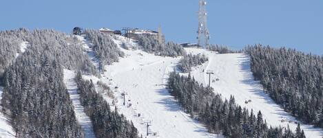 A snow-covered ski slope with ski lifts and buildings in the background.