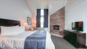 Una habitación de hotel con una cama grande, un televisor de pantalla plana, un aparador, una lámpara y un ventanal con cortinas.