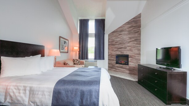 Een hotelkamer met een groot bed, een flatscreen televisie, een dressoir, een lamp en een raam met gordijnen.