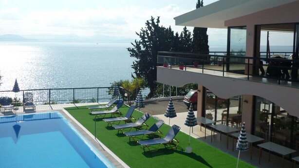 A poolside area with lounge chairs and umbrellas, overlooking a body of water and a mountainous landscape. - Karina (Corfu)