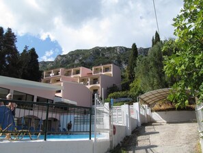 A hotel with a pool area, outdoor seating, and a view of the surrounding mountains. - Karina (Corfu)