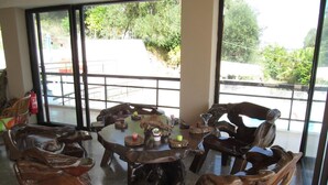 A wooden dining table with chairs in a room with large windows. - Karina (Corfu)
