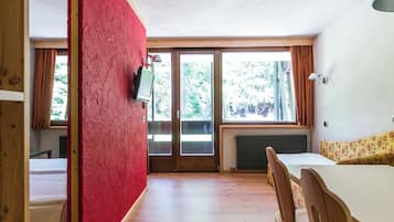 Une pièce avec un plancher en bois, une table à manger avec des chaises, un mur rouge et une fenêtre avec des rideaux.