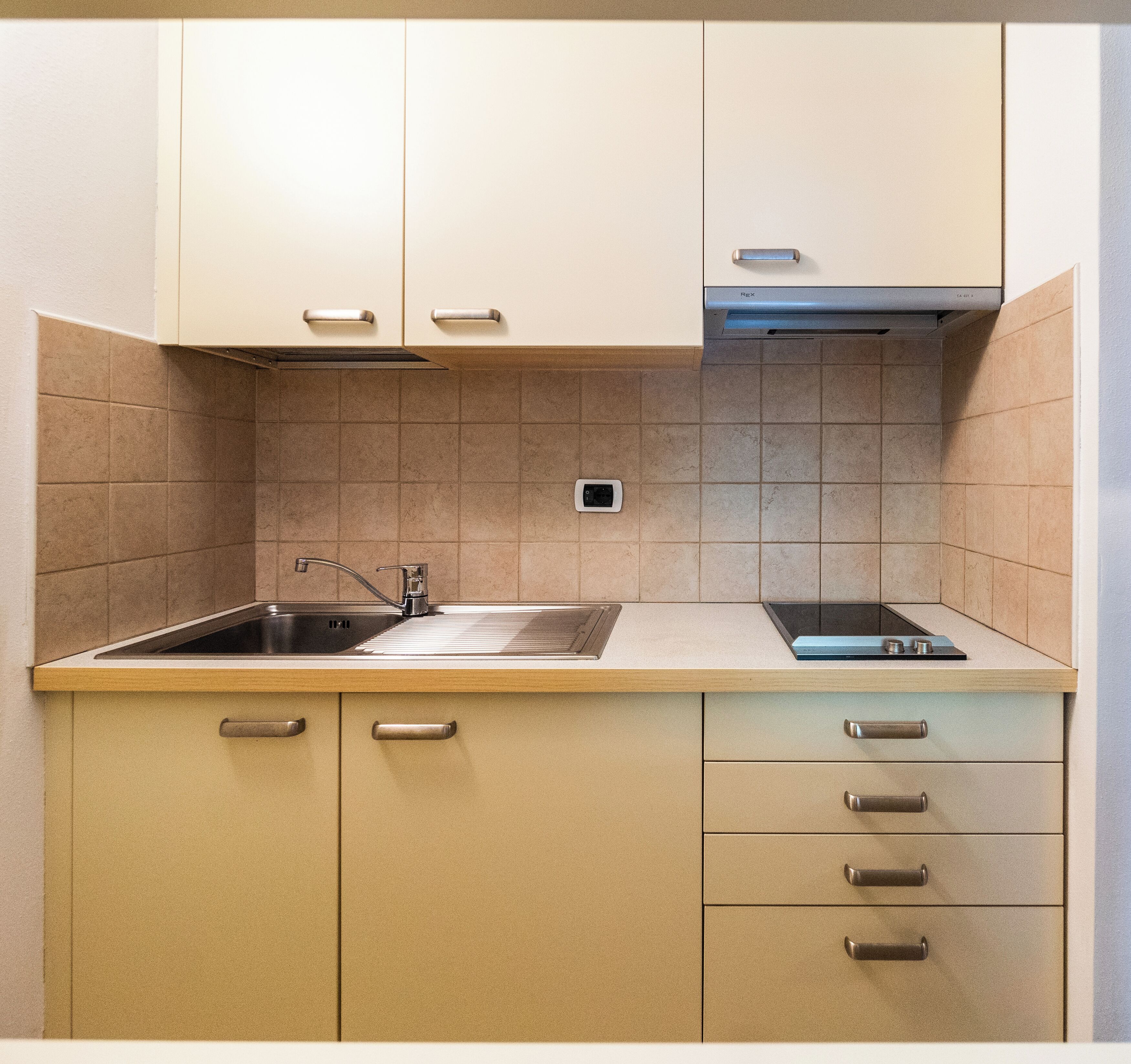 A kitchen with beige cabinets, a stainless steel sink, and a built-in stove.