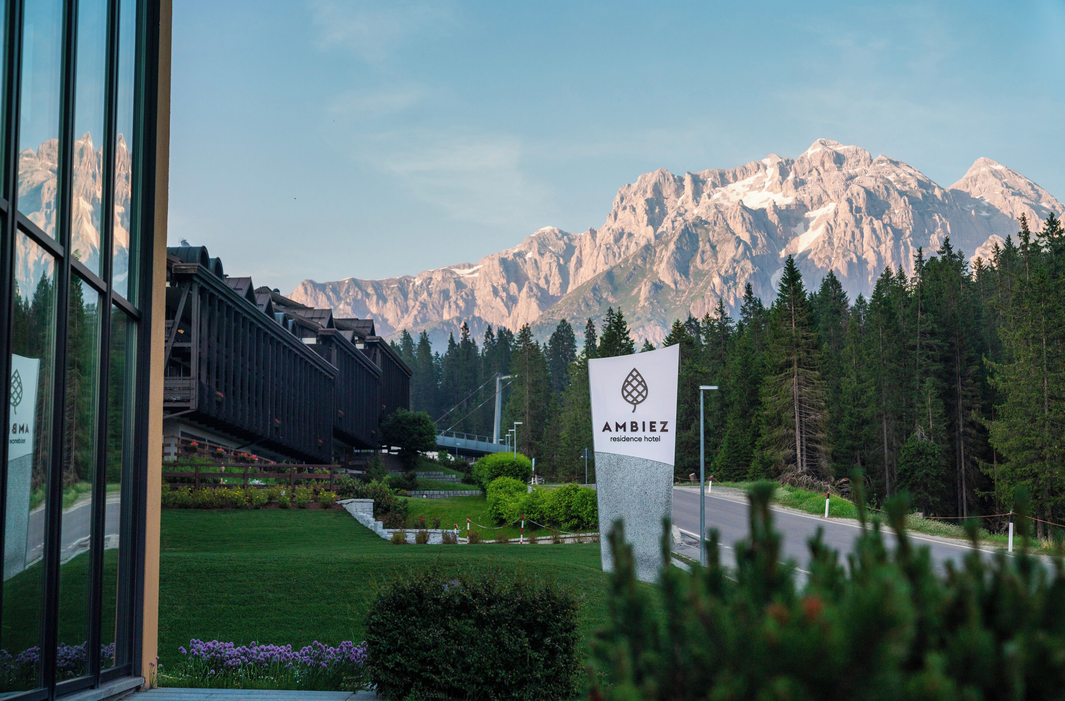 Ein modernes Gebäude mit Bergblick, einem Schild mit der Aufschrift 'Ambiez Residence Hotel' und einem gepflegten Rasen mit Blumen.