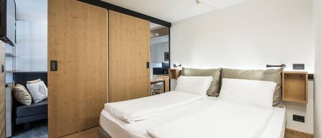 A modern bedroom with a large bed, wooden wardrobe, and a small desk area.