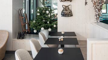 A modern dining area with a central table, four chairs, a Christmas tree, and wall decorations.