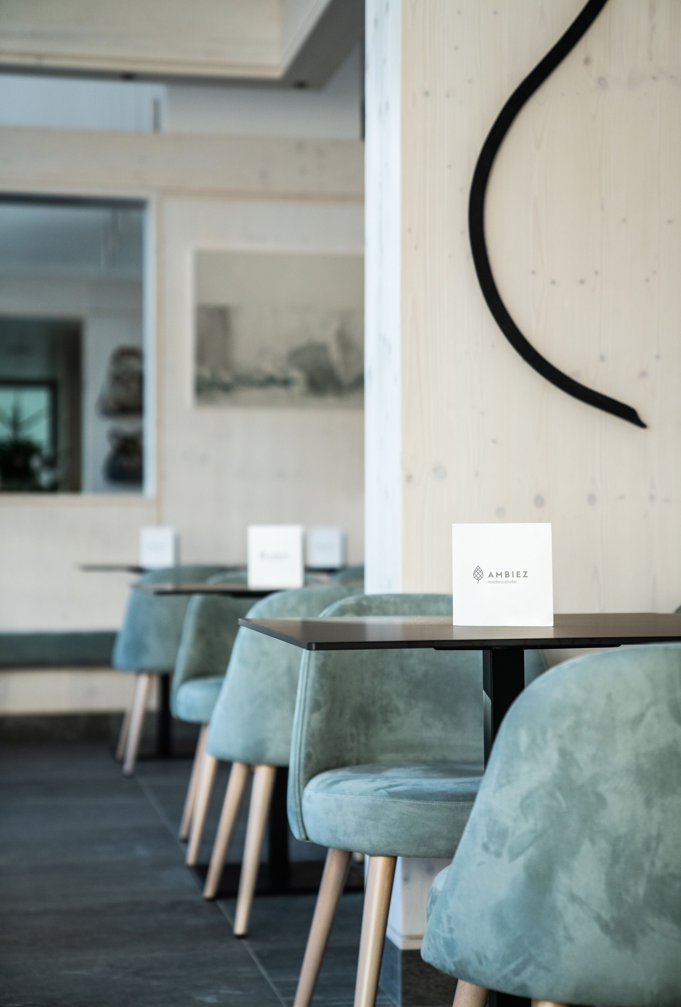 A modern interior with teal chairs and tables, a wooden accent wall, and a sign with 'AMBIEZ' logo.