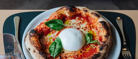 A pizza with a poached egg and basil on a plate, accompanied by a glass of red wine, set on a table with a placemat.