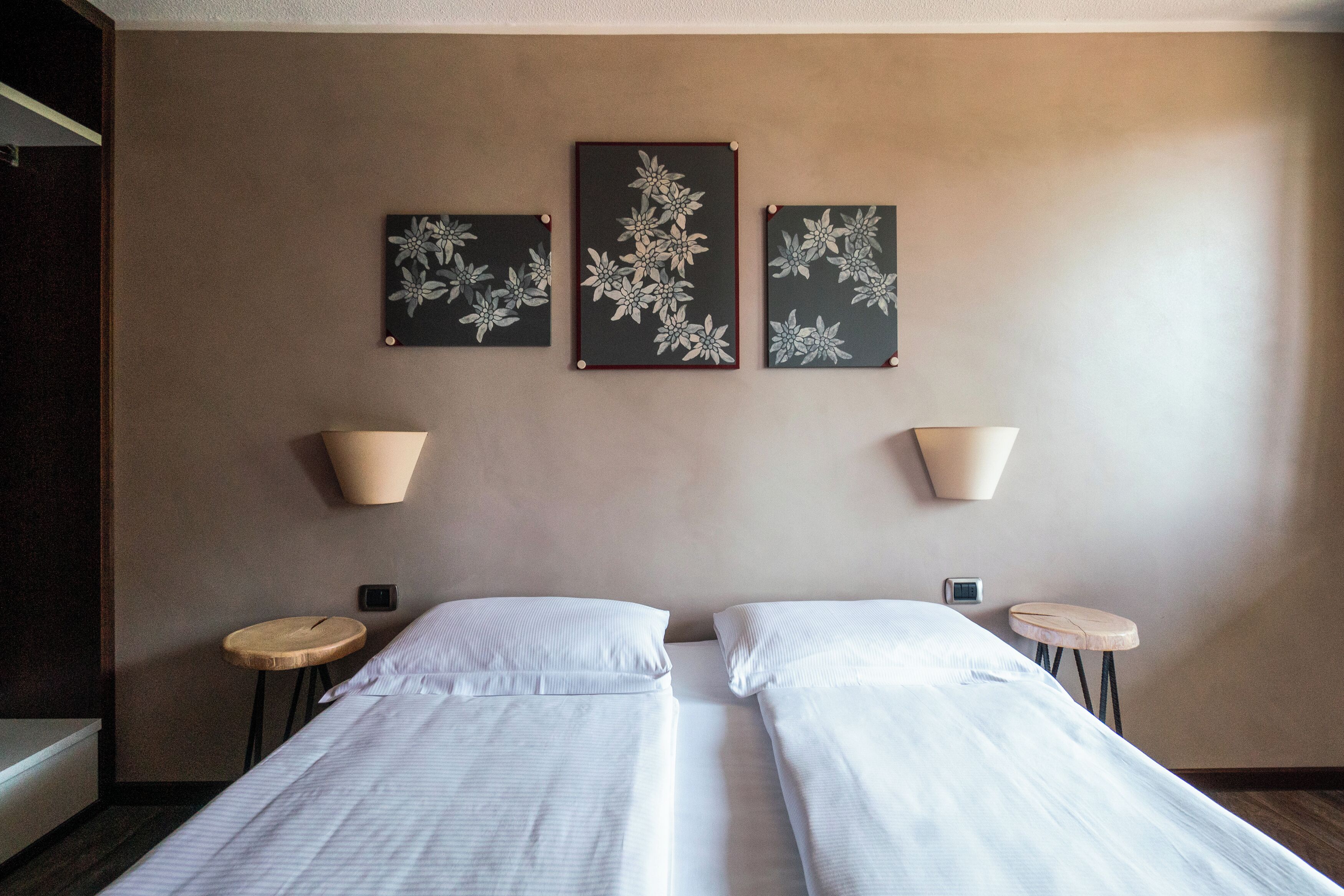 Habitación de hotel con dos camas, una lámpara fijada a la pared y una pequeña mesa redonda.
