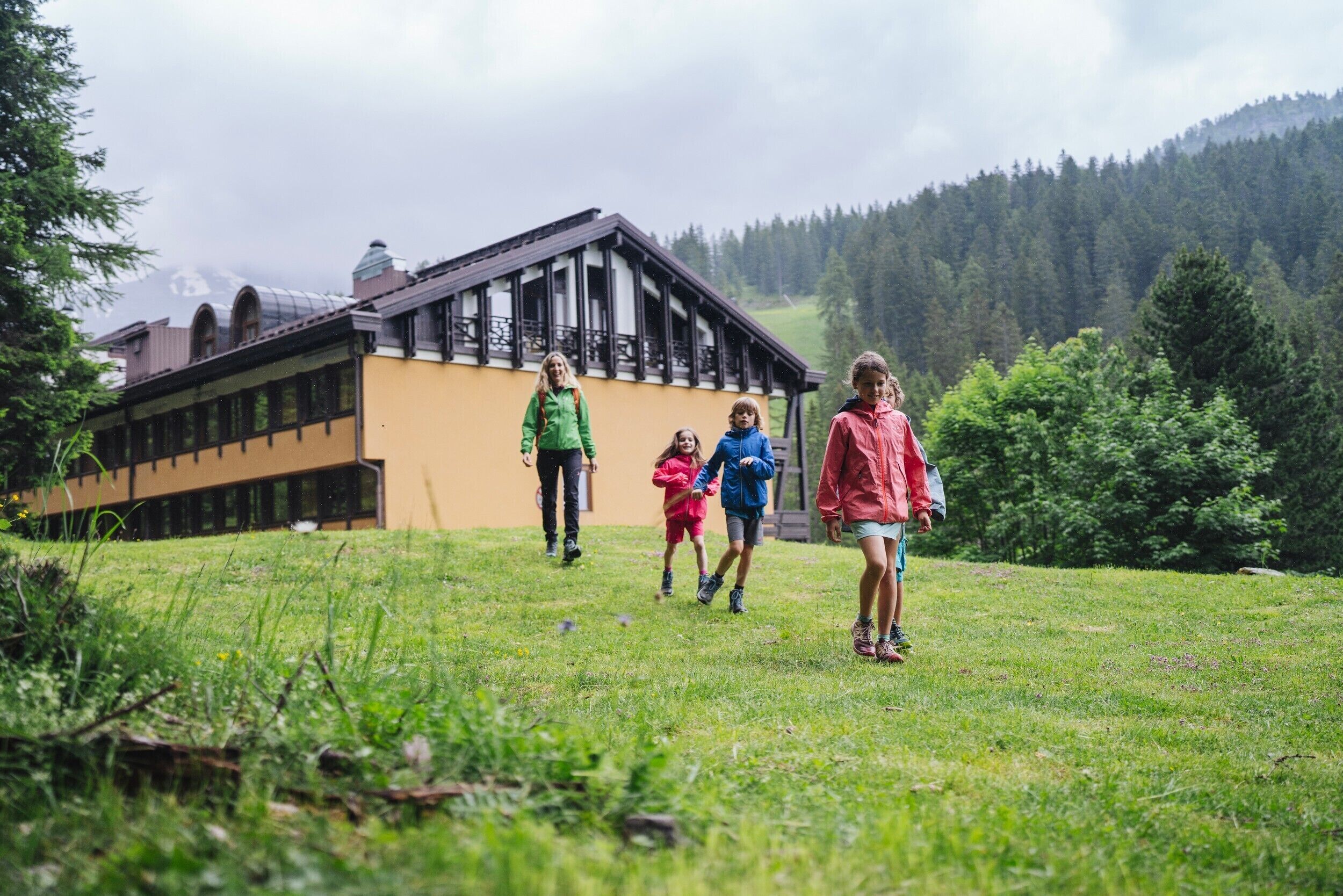 Un edificio con facciata gialla e rivestimenti in legno scuro, immerso nel verde tra prati e alberi.