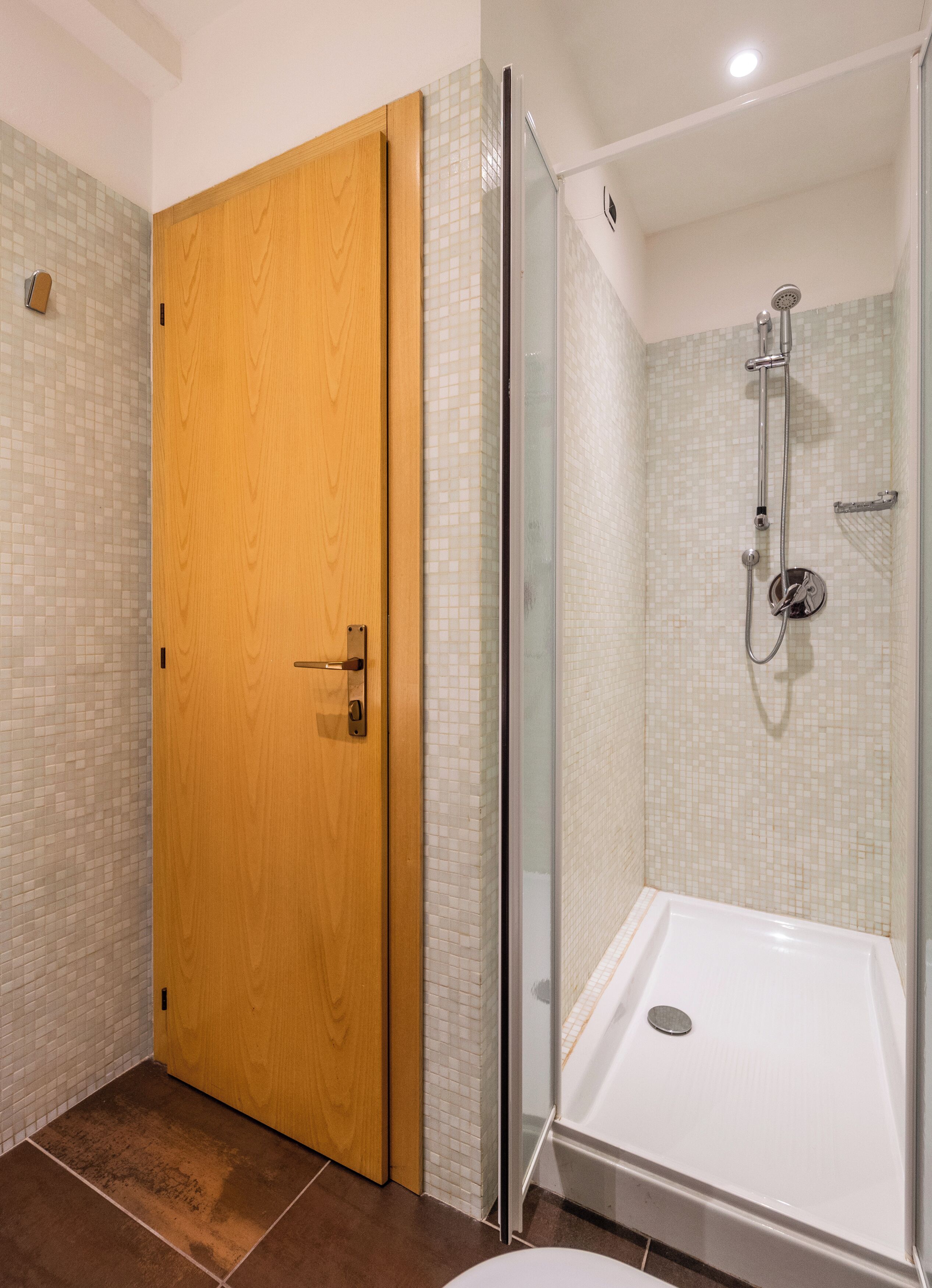 A bathroom with a wooden door, a glass shower enclosure, and a white bathtub.