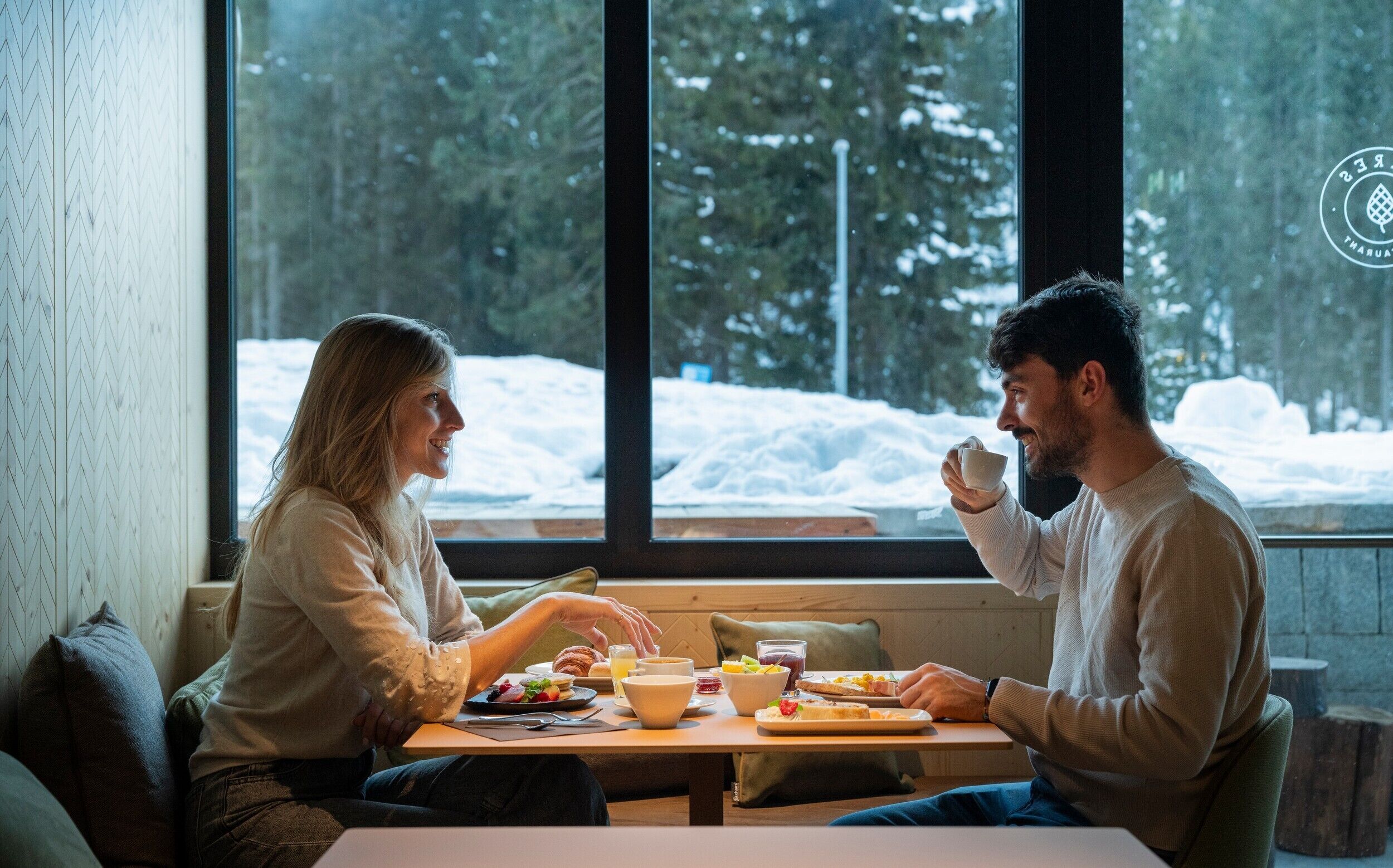 Ein Paar speist an einem Tisch mit Blick auf eine verschneite Landschaft durch große Fenster.