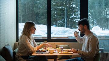 Un couple est assis à une table, près d’une grande fenêtre offrant une vue sur un paysage enneigé.