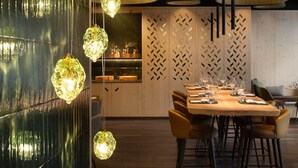 A modern dining area with a wooden table and chairs, hanging pendant lights, and a decorative wall panel. - Ambiez Residence (Pinzolo)
