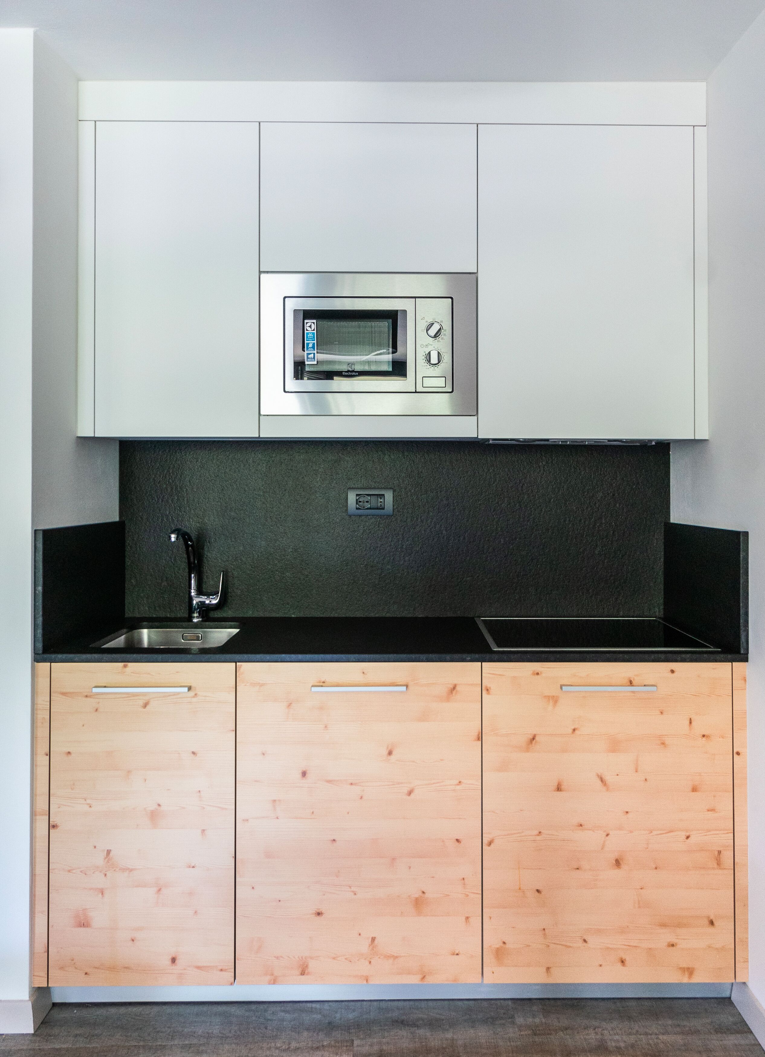 Una cucina compatta con forno a microonde integrato, lavello e mobili in legno.