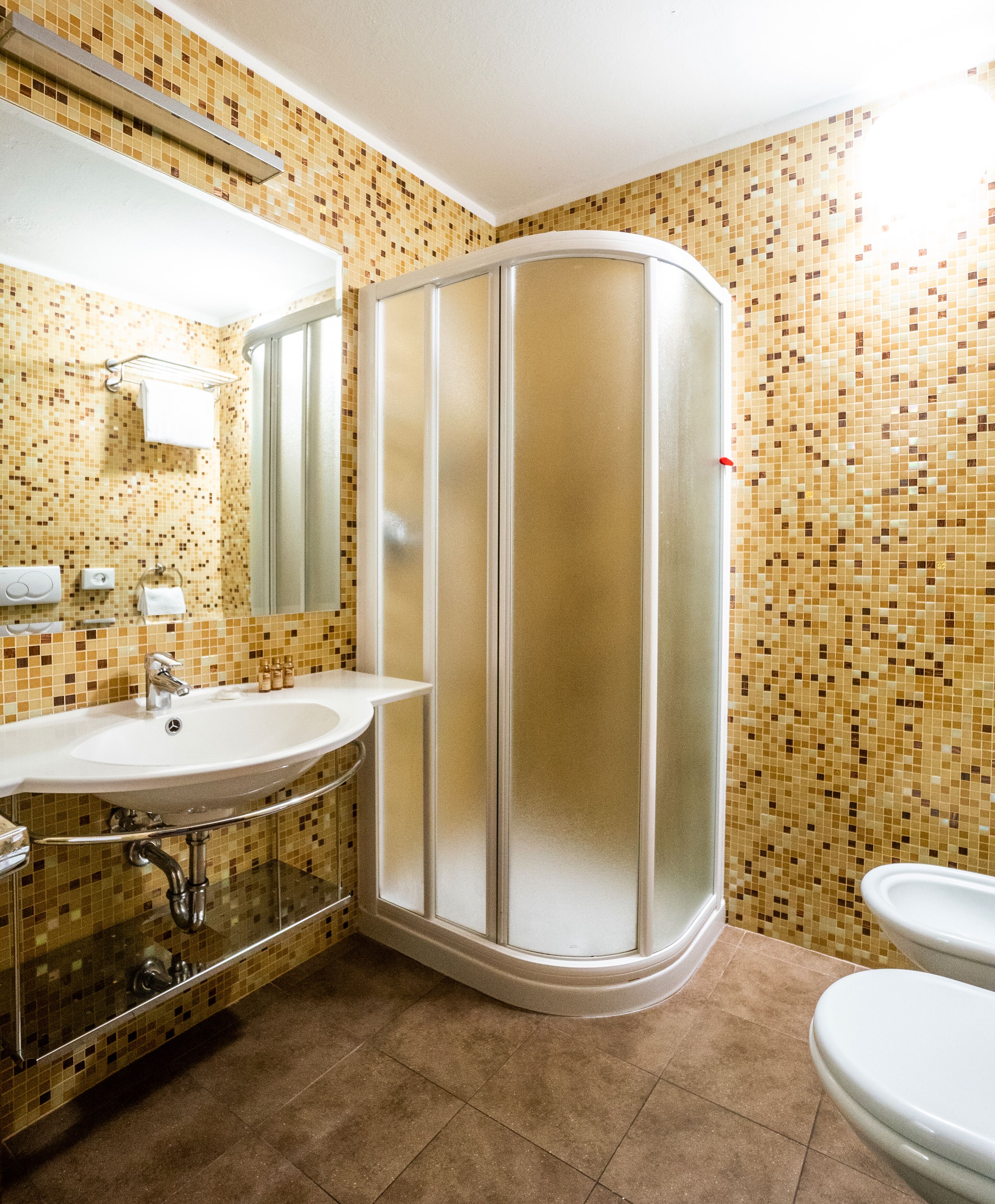 Un baño con ducha en esquina, lavamanos e inodoro.