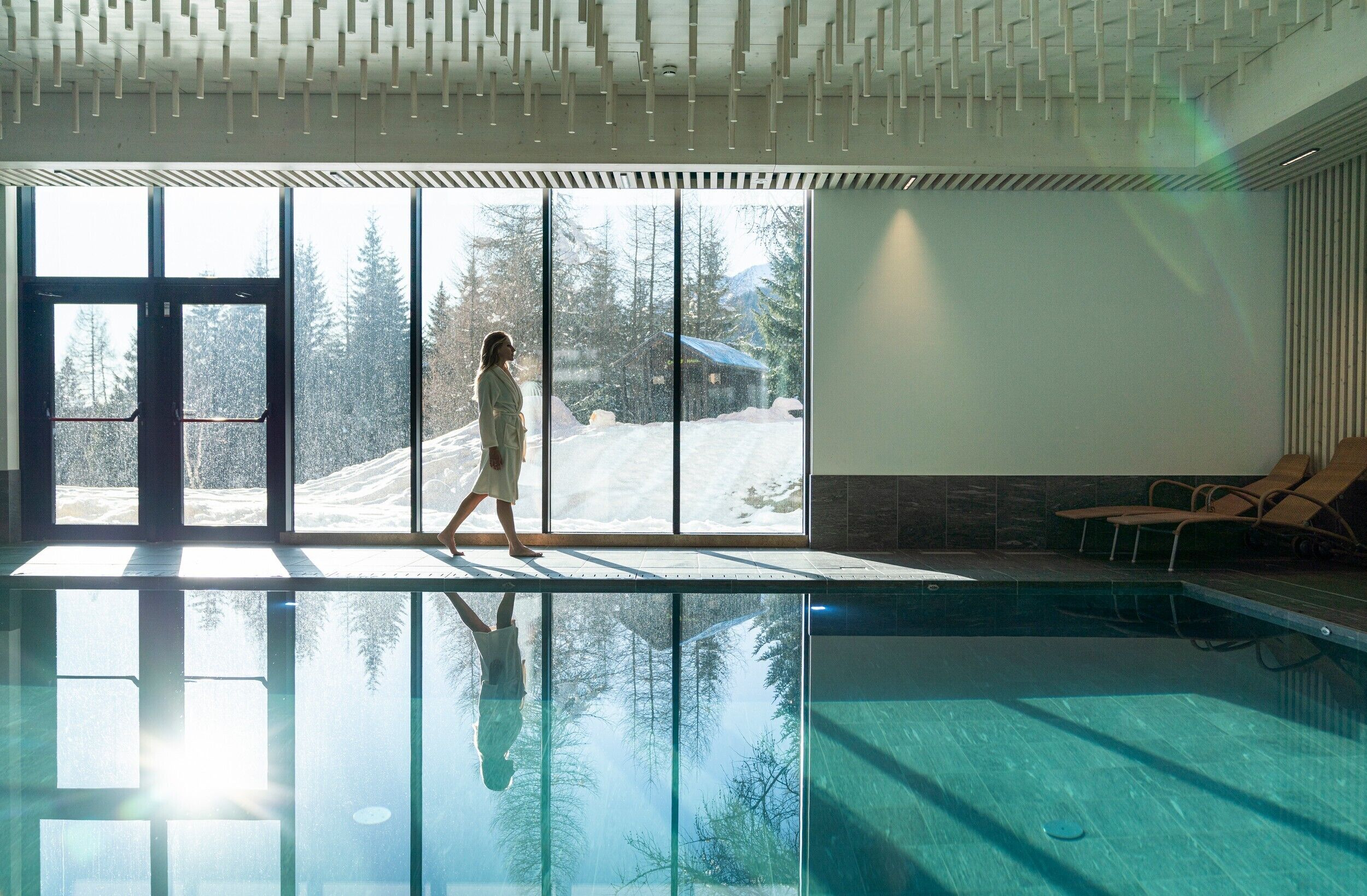 A swimming pool with a view of a snowy landscape through large windows.