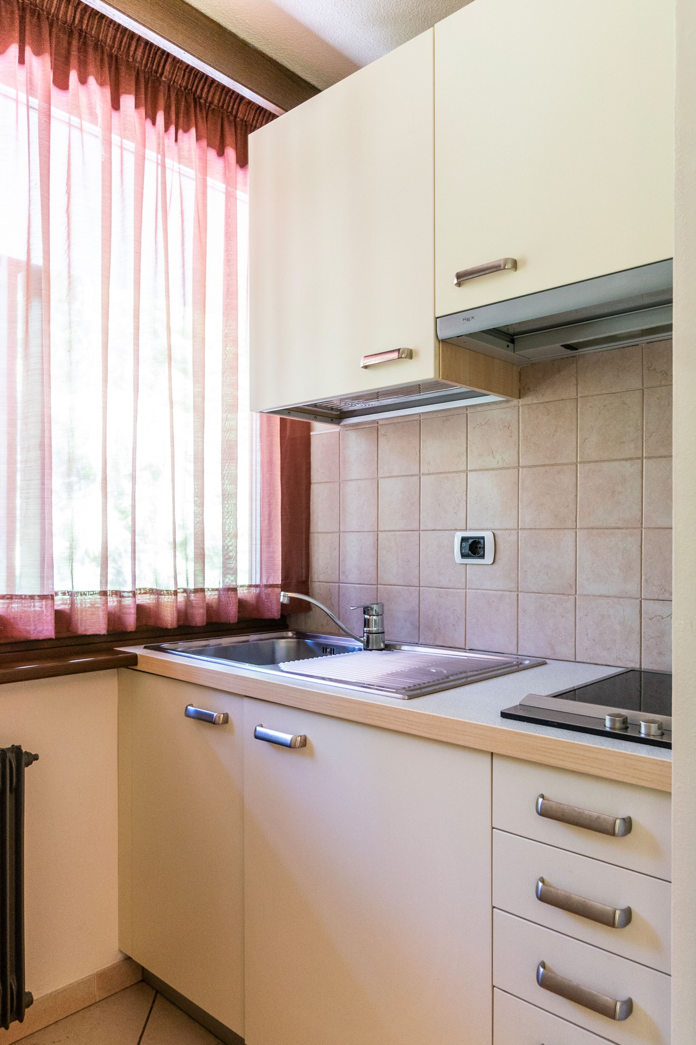 A kitchen with a sink, a stove, and a window with curtains.