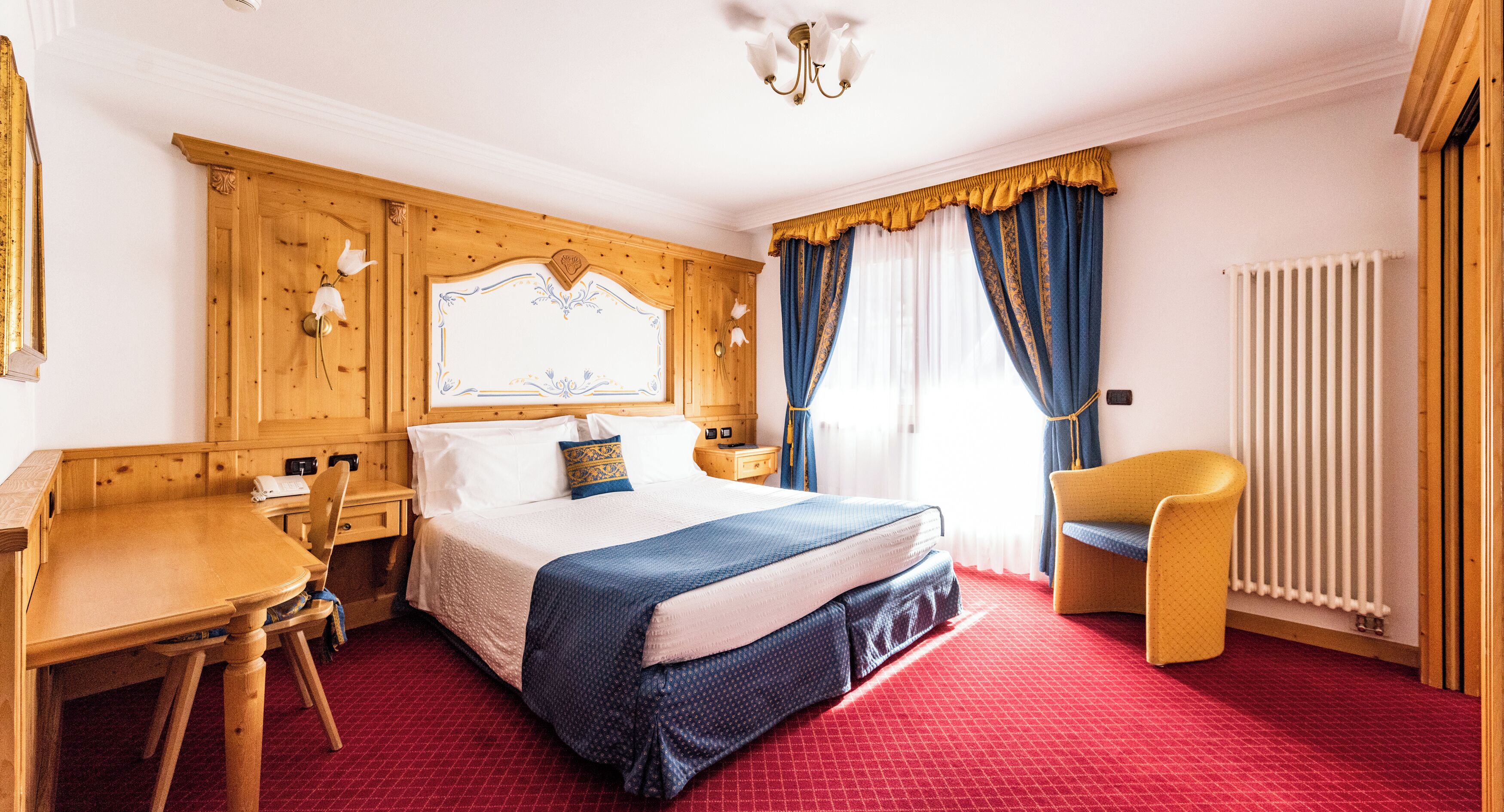 A hotel room with a wooden headboard, a bed with a blue and white bedspread, a wooden desk, a chair, and a radiator.