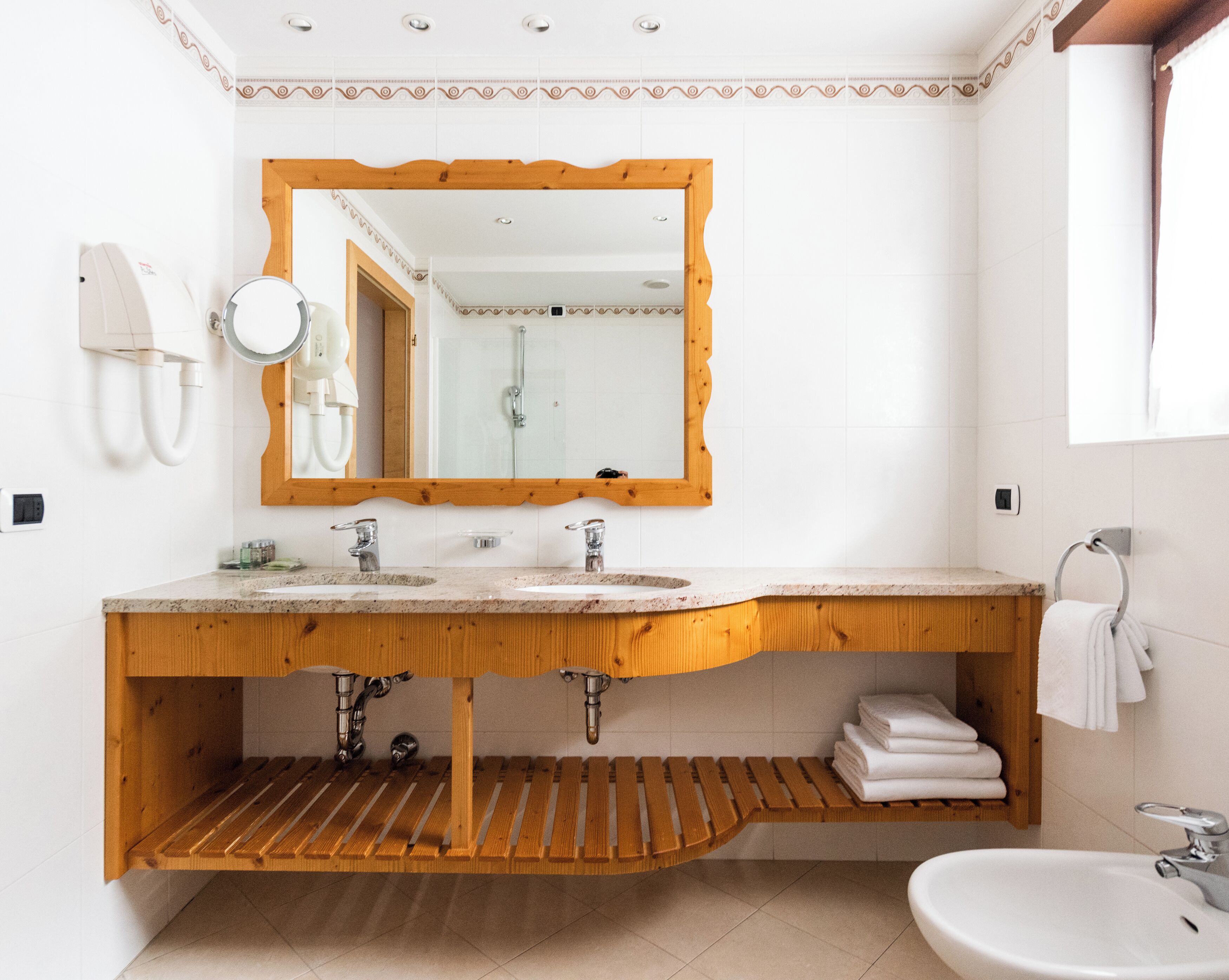 A modern bathroom with two sinks, a wooden vanity, a mirror, and a towel rack.
