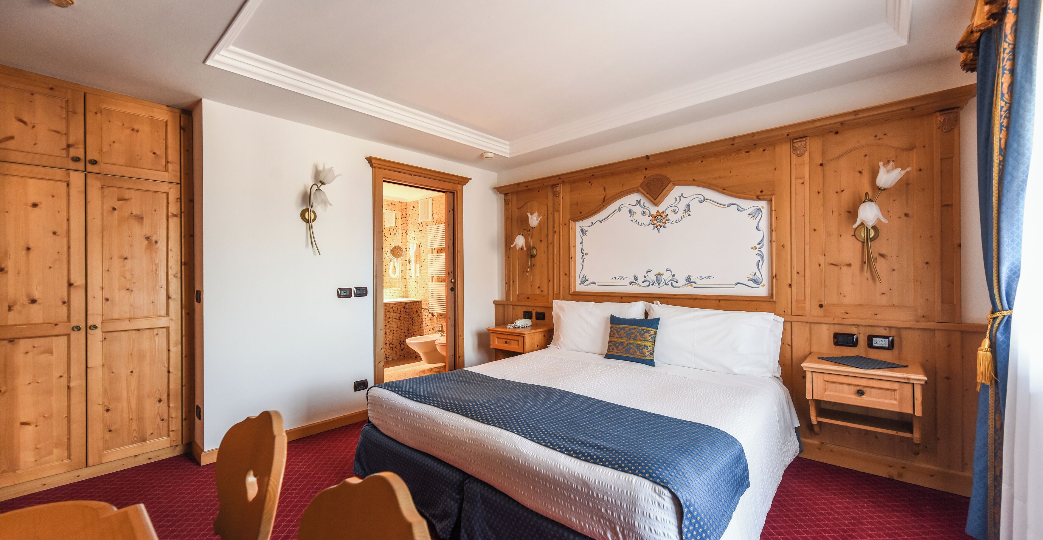 A hotel room with a large bed, wooden paneling, a wooden wardrobe, a bedside table, and a chair.