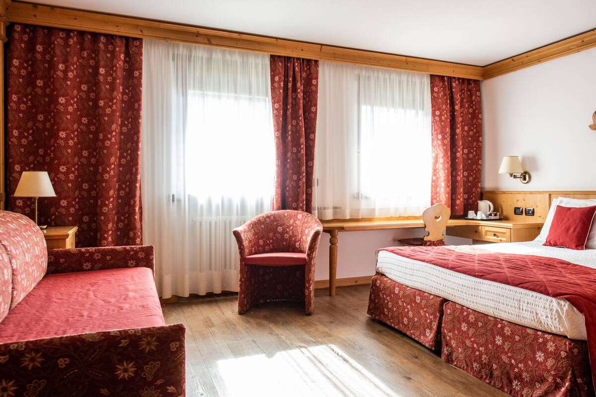 Una habitación de hotel con cama, escritorio, silla y ventana con cortinas.