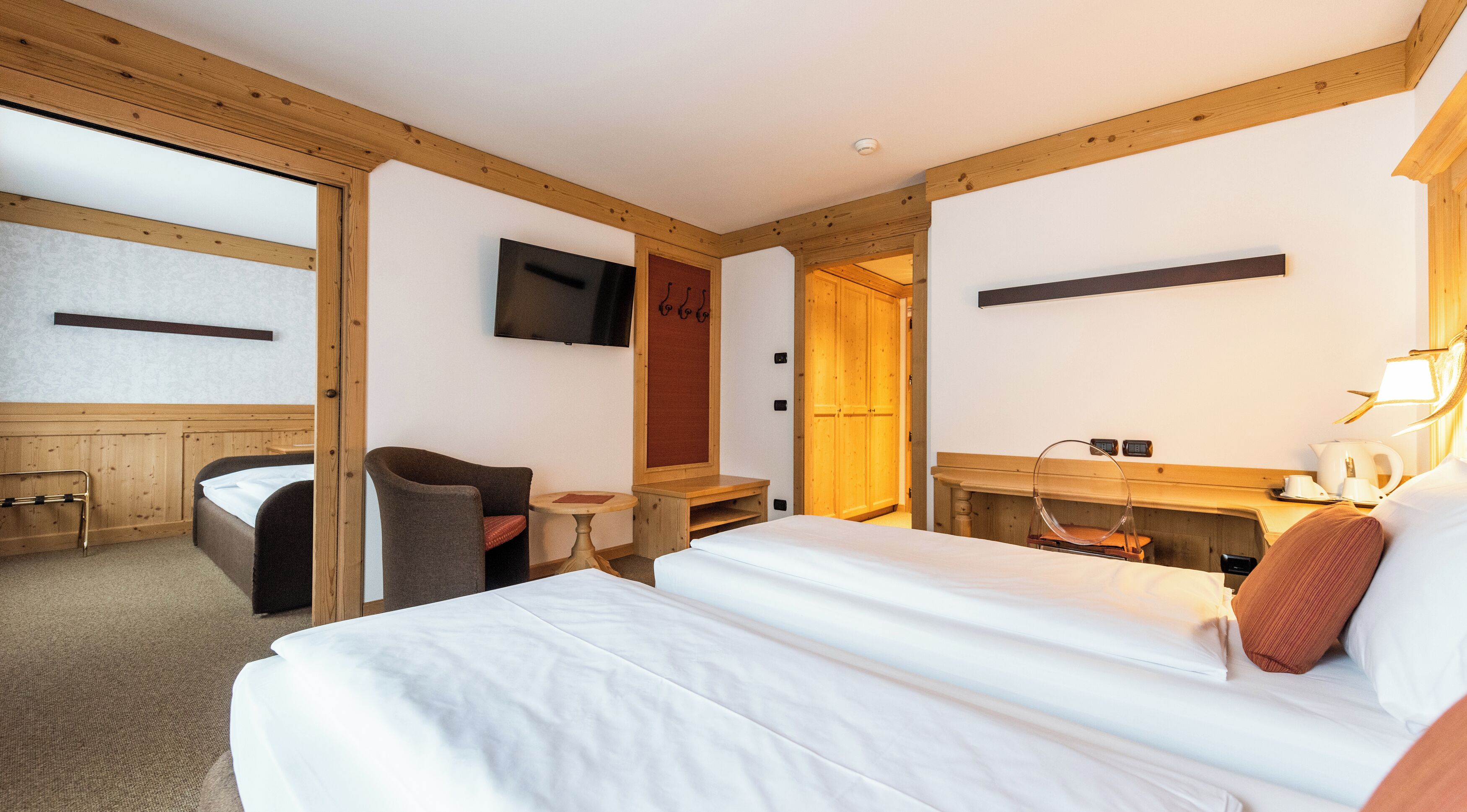 Une chambre d’hôtel comprenant un lit, une chaise, une petite table, un téléviseur fixé au mur et une armoire en bois.