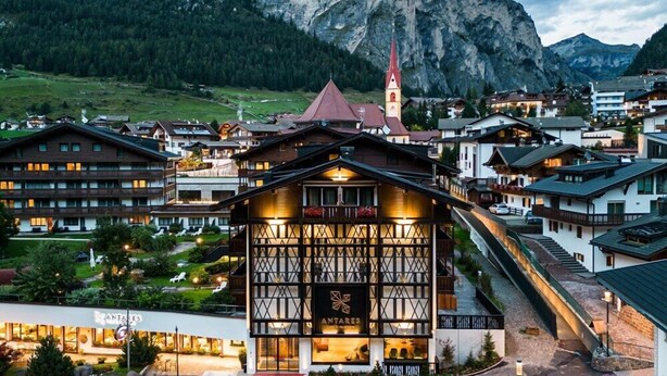 Ein Hotel im traditionellen Alpenstil, mit einem markanten Bergpanorama und einem Kirchturm.