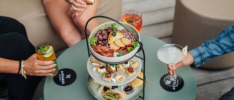 A three-tiered appetizer tray with various snacks and a drink on a round table.