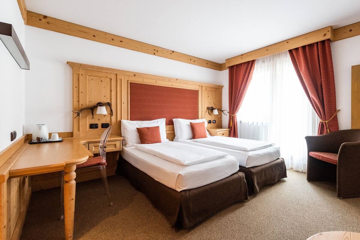 Habitación de hotel con dos camas, un escritorio de madera, una silla y una ventana con cortinas.