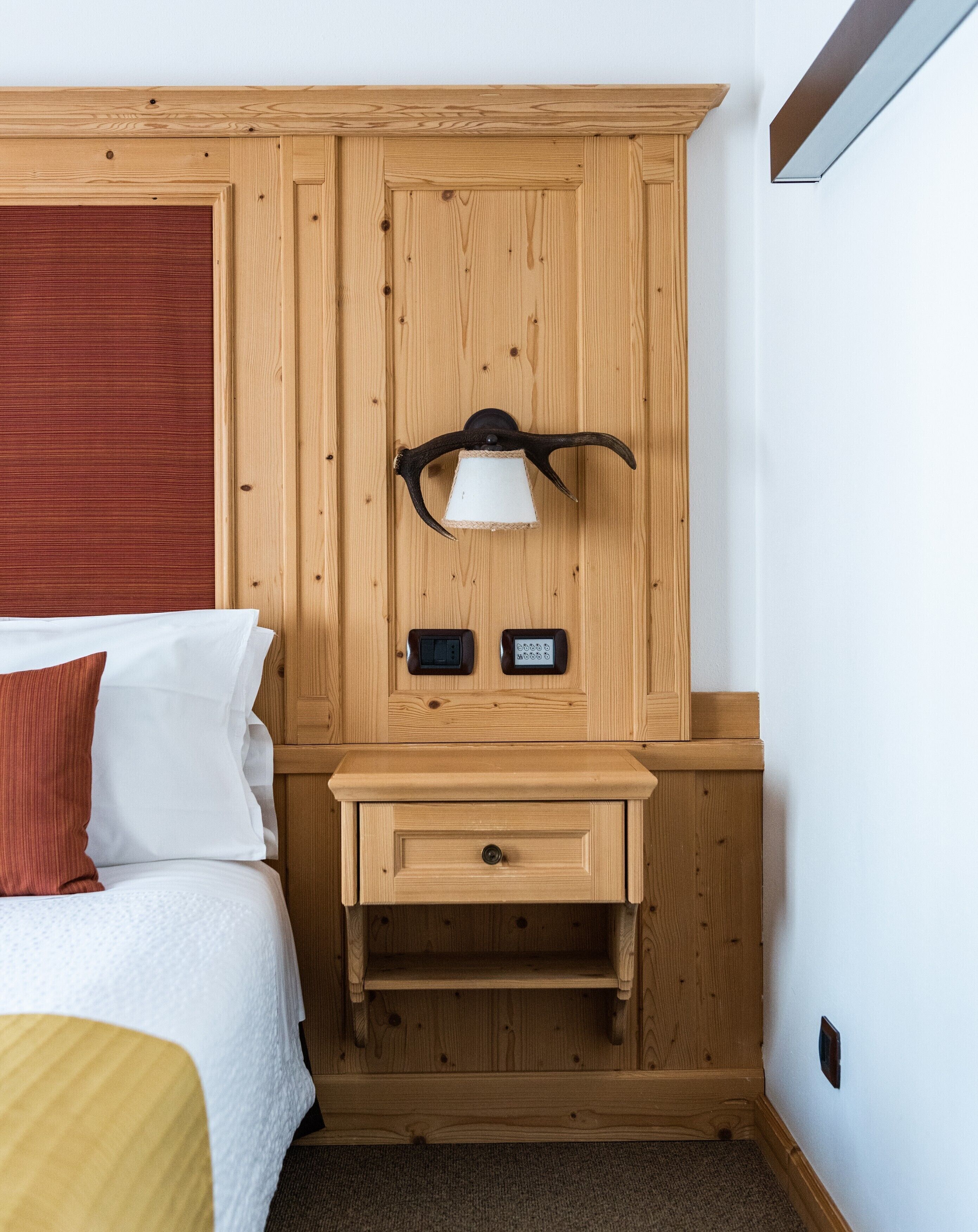 A wooden room with a bed, a nightstand, a lamp, and a thermostat.
