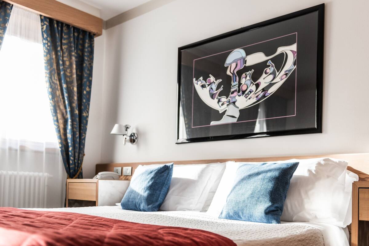 Habitación de hotel con una cama, una mesita de noche, una lámpara y una obra de arte enmarcada en la pared.