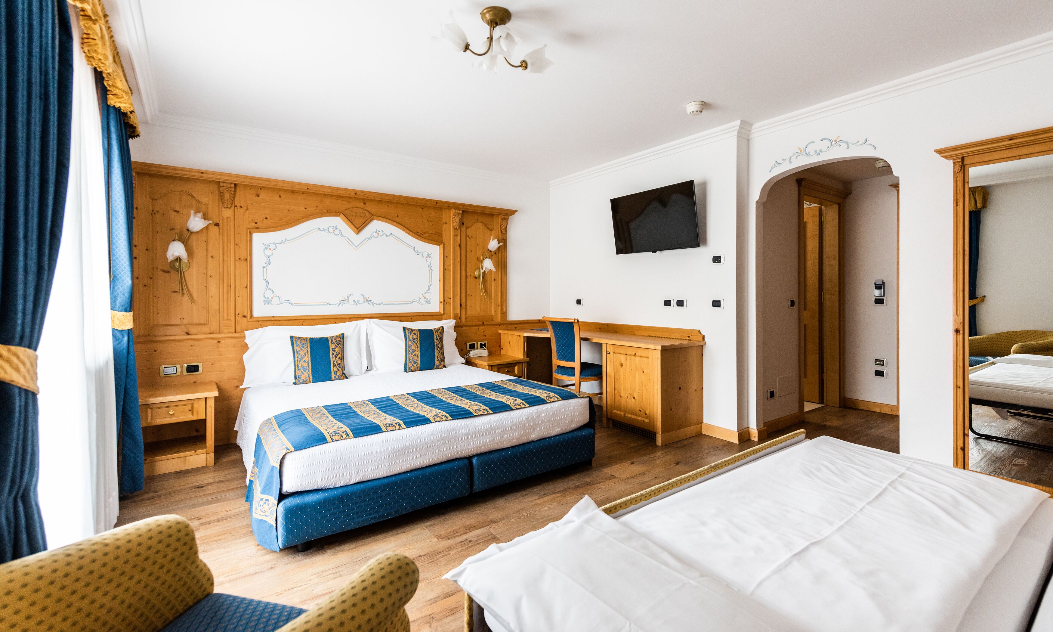 A hotel room with a large bed, a desk, a TV, and a wooden wardrobe.